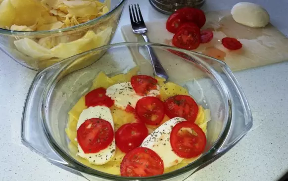 Zapékací misku vymažeme máslem a na dno položíme část brambor. Na ně navrstvíme rajčata pokrájená na kolečka, mozzarellu a posypeme bazalkou. Poté vrstvy opakujeme. Končit bychom měli bramborami, na které položíme poslední kousky mozzarelly a několik kousků másla.