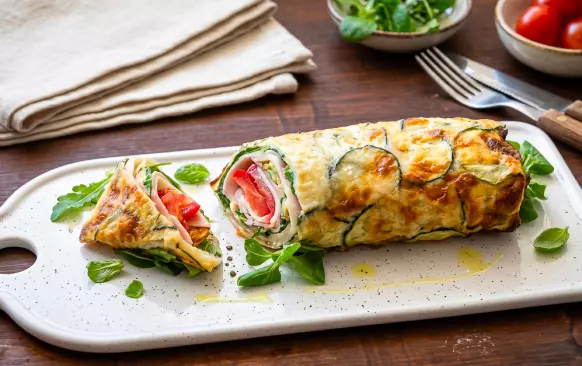 "TORTILLA"
Cuketu omyjte a nakrouhejte na tenká kolečka pomocí mandolíny nebo široké ploché škrabky.
Nasypte je na bavlněnou utěrku, výrazněji osolte a za občasného promnutí nechte vypotit 10-15 minut.
Cuketové plátky otřete od přebytečné vlhkosti a pak rovnoměrně rozložte na plech vyložený pečicím papírem, tak aby se na okrajích vzájemně lehce překrývaly. Na 2 porce vychází jeden plný plech o rozměrech cca 42 × 33 cm.
Rozmixujte vejce a cottage sýr. Směsí zalijte připravené cuketové plátky a navrch rovnoměrně posypte jemně nastrouhaným nízkotučným sýrem.
Vložte do trouby vyhřáté na 180 °C (horkovzduch) a pečte dozlatova cca 20 minut.
Pak nechte zchladnout a rozkrojte na 2 pláty.
NÁPLŇ
Upečené cuketové "tortilly" posypte polníčkem, rukolou a/nebo baby špenátem.
Navrch rozložte plátky šunky (pro vegetariánskou verzi nakoukněte do TIPŮ na konci receptu), lehce je potřete majonézou a pokryjte plátkovým nebo strouhaným sýrem.
Přidejte na plátky nebo na kostičky nakrájená rajčata a vše pevně smotejte.
Podávejte jako hlavní chod nebo rozkrojené na dílky jako snack. S sebou na cesty tortilly pevně zamotejte do pečicího papíru nebo alobalu.
Jídlo chutná nejlépe do pár hodin po přípravě. V případě potřeby lze ale předem upéct cuketové tortilly a ty zakryté až několik dní uchovat v lednici (pro zamrazení se nehodí).
TIPY
Na přípravu zvolte mladé cukety s méně výraznými semínky.
Místo cottage sýru lze použít například tvaroh nebo mozzarellu.
Nízkotučný sýr v tortille je použitý záměrně. Díky němu placka zůstane pružná a nebude zbytečně mastná.
Místo šunky lze použít na plátky nakrájená pečená kuřecí prsa nebo trhané maso. V případě vegetariánské či bezmasé verze tortillu naplňte například opečeným halloumi sýrem, pečenou hlívou či míchanými vejci.
Pro výraznější chuť můžete majonézu nahradit její směsí s jogurtem, česnekem a bylinkami. Skvělé bude i guacamole.
Pokud naplněné tortilly budete chtít podávat později, nakrájená rajčata nasolte a nechte vykapat v sítu. Zamezí to jejich pozdějšímu rozmočení.
Náplň můžete libovolně obměňovat podle své chuti a obsahu lednice.